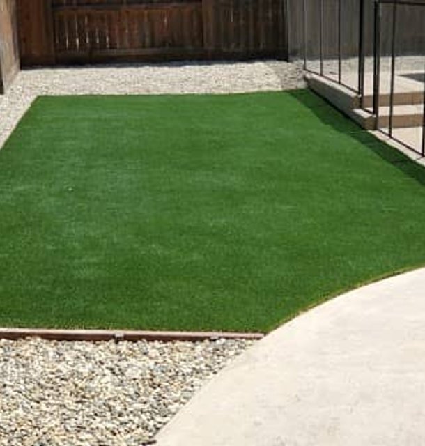 Synthetic turf yard bordered with river rock and concrete